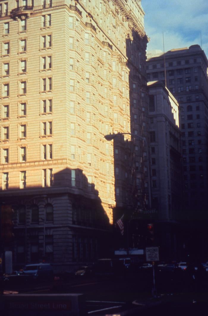 The tall stone facade of the Bellevue-Stratford Hotel in late sun, with a street lamp, an American flag, a Chestnut Street sign and a Broad Street Line subway sign at street level